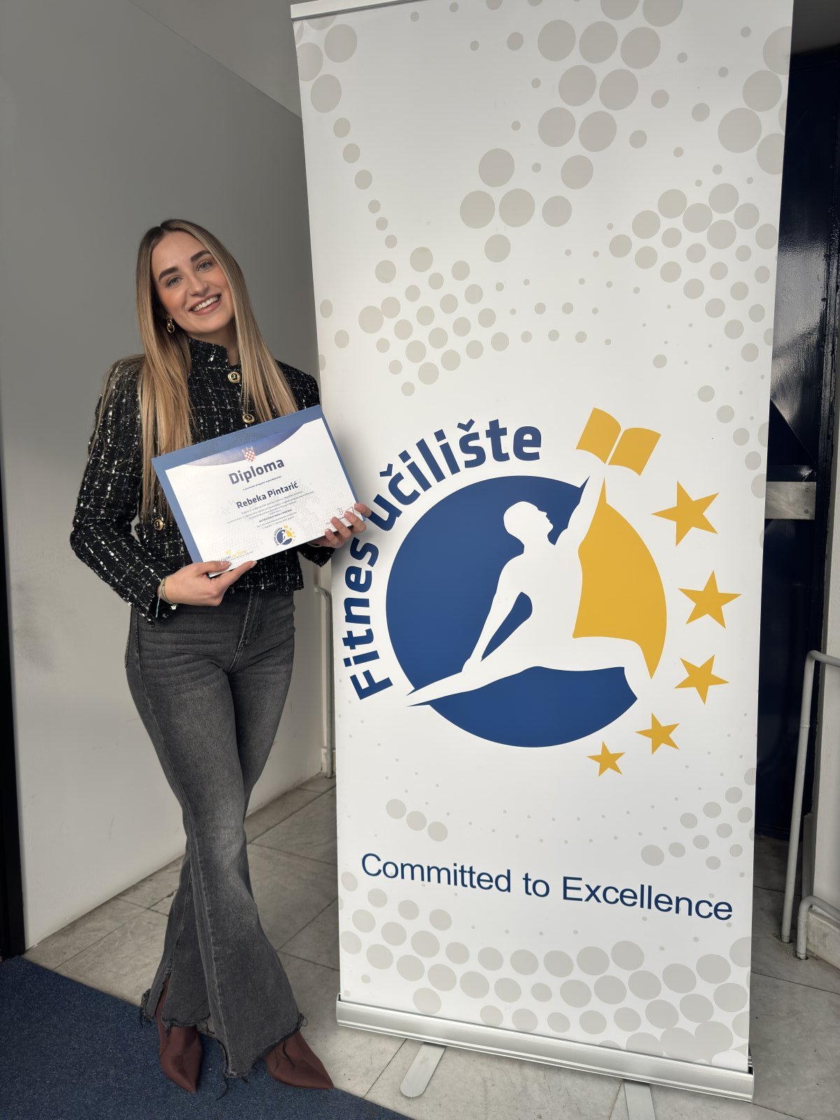 Rebeka Pintarić ponosno drži diplomu Fitnes učilišta ispred roll-up bannera